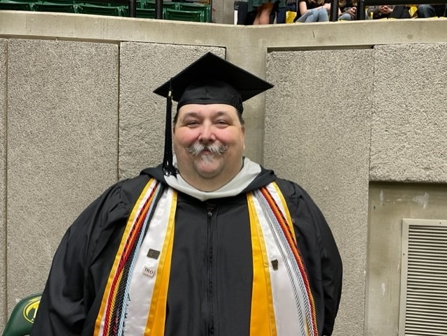 Smiling man with mustache poses in graduation regalia