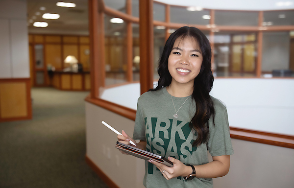 Student smiling at camera while she holds a tablet on the 3rd floor of the library