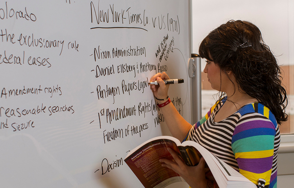 Woman writing on whiteboard with an open book in her other hand